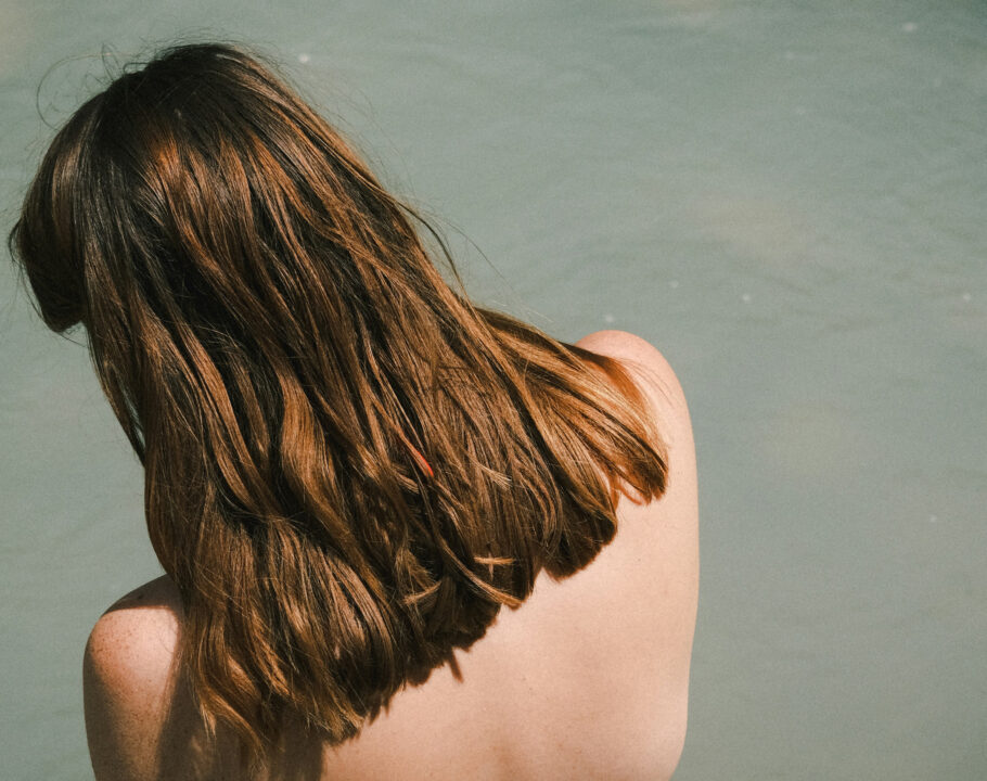 back view of woman with brown hair sitting on dock