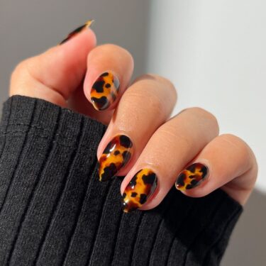 A close-up of a woman's hand with oval nails with tortoise shell print