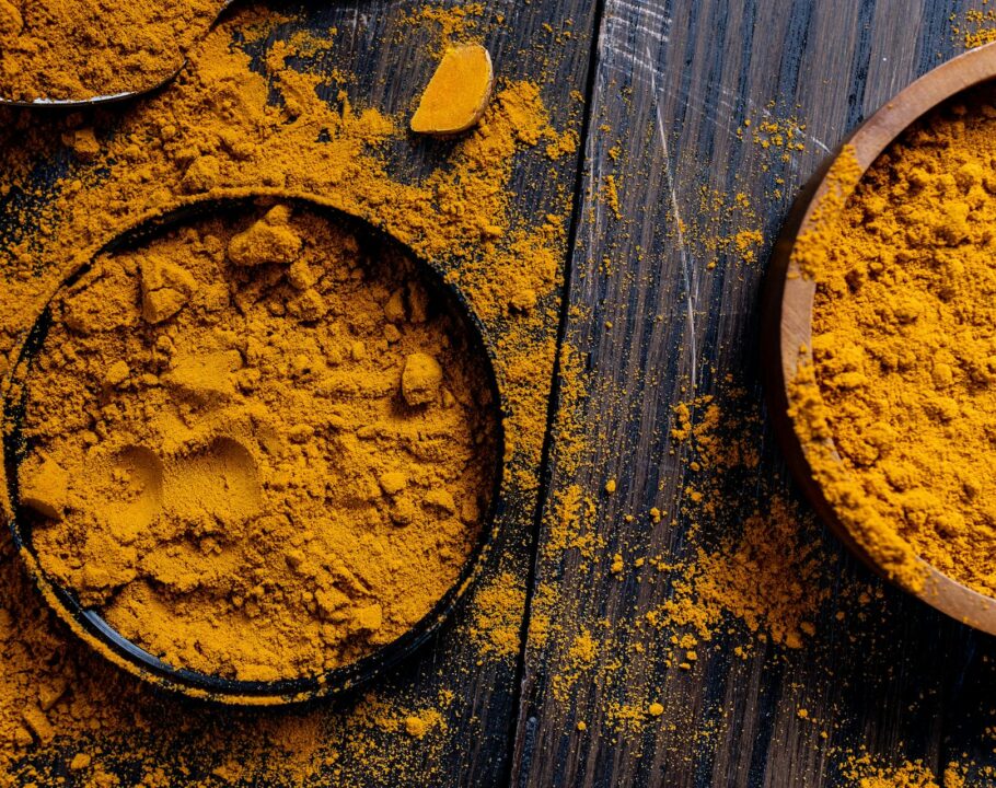 Two bowls of grounded turmeric on a table with some turmeric powder on the table