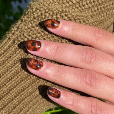 A close-up of a woman's hand with short tortoise shell nails