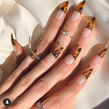 A close-up of a woman's hands on top of each other with half moon design nails with tortoise shell print