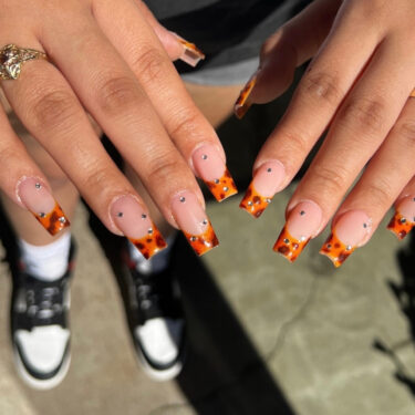 A close up of a woman's square nails with tortoise shell tips and her feet in sneakers blurred in the background