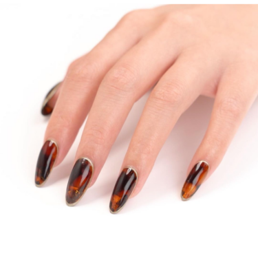 A close up of a woman's hand with tortoise shell nails with silver embellishments