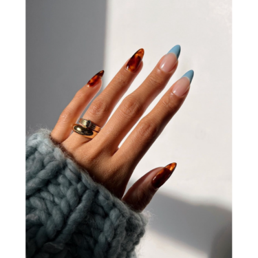 A close up of a woman's hand with long nails with mixed design and two rings on her ring finger